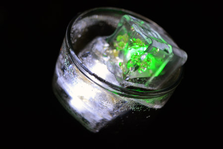 Ice cubes in a glass jar on a black background close-up. Transparent glowing cubes of white and...