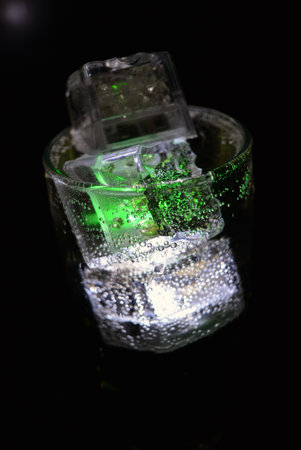Ice cubes with green light on a black background. Macro shot. Transparent glowing cubes of white and...
