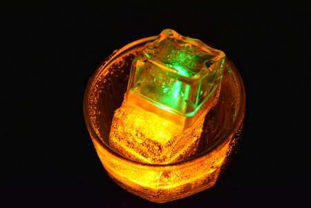 Beautiful bright serving of a drink in a glass with glowing ice for fun, a party, a holiday. Transparent glowing cubes of yellow and green color with a sparkling drink are locatedの写真素材
