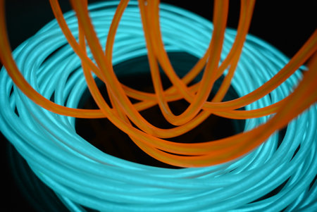 Fiber Optic cables in blue and orange color, computer generated abstract. Bright glowing electroluminescent wires, yellow, orange, blue, sky blue, turquoise thick light lines.の写真素材