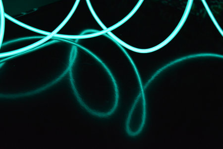 Green neon light on a black background, close-up of photo. Bright glowing electroluminescent wires, light green, green, blue, sky blue, turquoise thick light lines.の写真素材