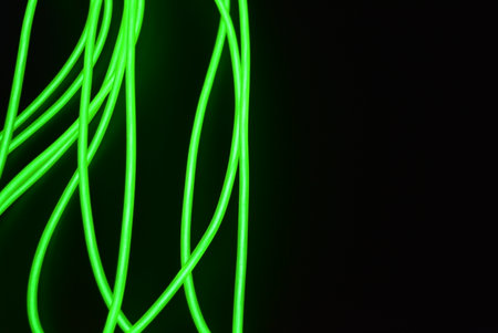 Green neon lines on a black background. Neon lines in motion. Neon chaotic lines are arranged in...