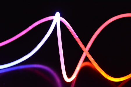 Abstract light lines on a black background in the form of a wave. Multicolored light, beams of light pass along plastic twisted tubes. Art glowing plastic, fibers.の写真素材