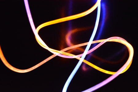 Abstract light painting on a black background - long exposure photo. Beautiful and unusual graphic. Multicolored light, beams of light pass along plastic twisted tubes.の写真素材