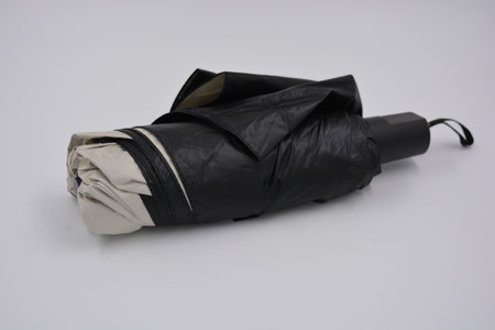 Black umbrella on a white background. Close-up. Isolated. Beige, gold, white, light umbrella with black handle, light cover, black lining from water and rain.の写真素材