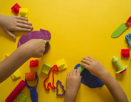 The child molds from colored plasticine. Yellow background. Materials and tools for modeling. Children's hands.の写真素材