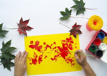 A child paints a picture of an autumn leaf with paints. Children's hands. Favorite hobby, materials for creativity.の写真素材