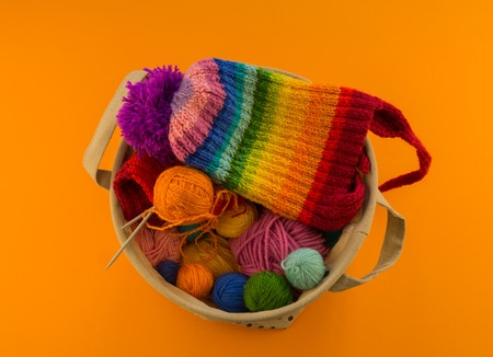 Rainbow cap made of wool on an orange background. Copy space. View from above. Striped knitted warm hat with pompon.の写真素材