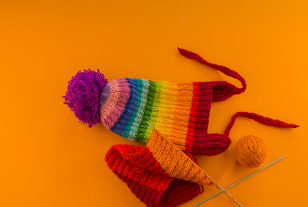 Rainbow cap made of wool on an orange background. Copy space. View from above. Striped knitted warm hat with pompon.の写真素材