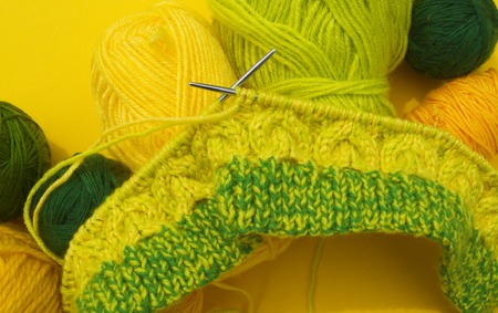 Yellow and green coats of wool lie on the table. Favorite hobby is knitting. Home cosiness.