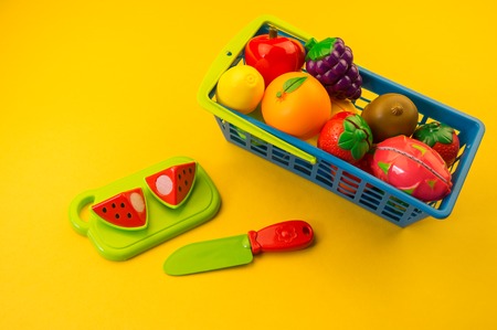 Children's toy plastic fruit in a basket on a yellow background. Kindergarten developmentの写真素材