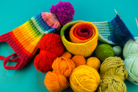 Knitting a rainbow scarf and hat. Basket with balls of wool, knitting needles. Blue background. Favorite work is a hobby.の写真素材