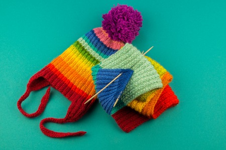 Knitting a rainbow scarf and hat. Basket with balls of wool, knitting needles. Blue background. Favorite work is a hobby.の写真素材