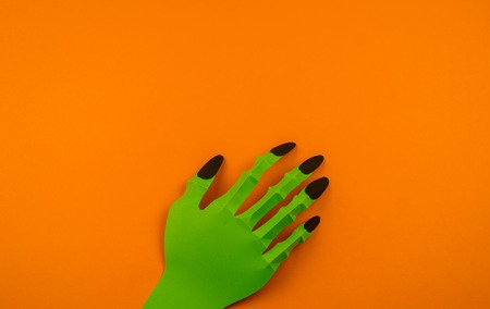 Orange background with collection of Halloween objects origami overhead view. Green monster hand. Feared party decor. Handwork.の写真素材