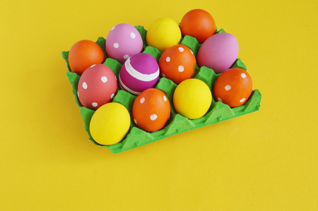 Easter eggs in a tray for eggs a stand. Yellow background. Colors are green orange yellow and pink