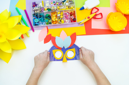 A child makes a bird mask out of paper. Master class crafts. Tropical Parrot. School, kindergarten. Children's hands cut, glue, make.の写真素材