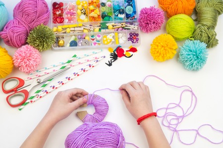 The child is engaged in a favorite hobby. The kid makes a pom-pom from a woolen thread monster. Holiday toy gift. Creativity with children. School kindergarten. Material for crafts.の素材 [FY310122560000]