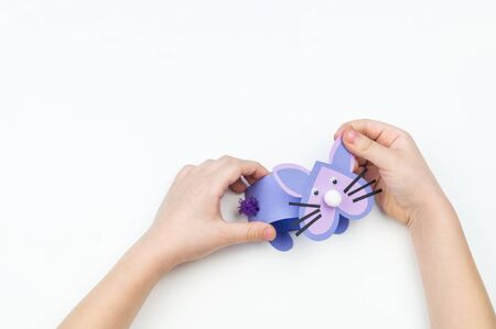 Child makes an Easter bunny out of paper. Children's hand. White background. Holiday Easter light....