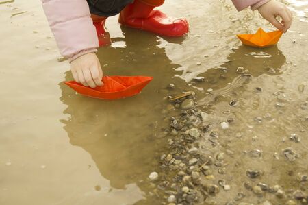 A boat made of colored paper in the snow. Origami handicraft. Spring the river is melting. Bright...