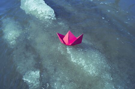 A boat made of colored paper in the snow. Origami handicraft. Spring the river is melting. Bright colorの写真素材