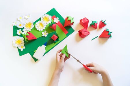 Origami strawberry made of craft paper. Learning at home. Kid diy. Hands of the child master creativity. White background.の写真素材