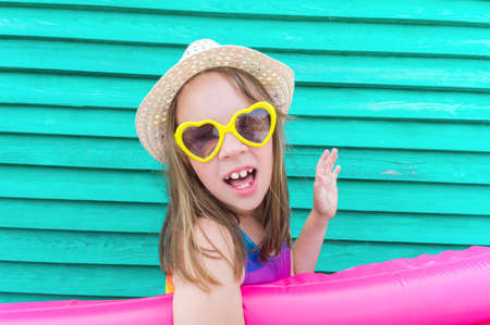 Girl with an inflatable duck. Baby in hat and glasses on a wooden background. Active holidays with...