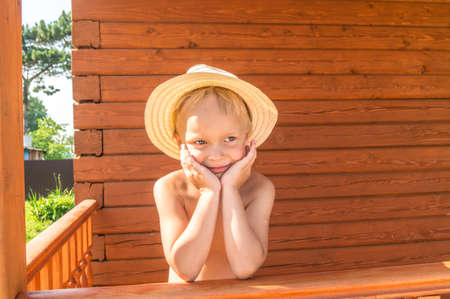 Boy in a straw hat on a wooden background. Farmer village. Warm tones of tanned skin.