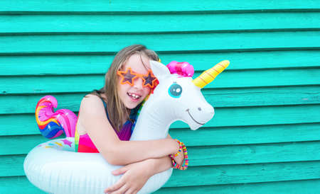 Girl circle unicorn. Baby in hat and glasses on a wooden background. Active holidays with family on the beach pool. Emotional kidの写真素材