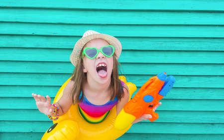 Girl with a water gun. Baby in hat and glasses on a wooden background. Active holidays with family...