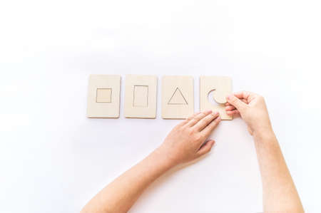 Montessori material math form flat lay. Children hand sort. Wooden tray on a white background.