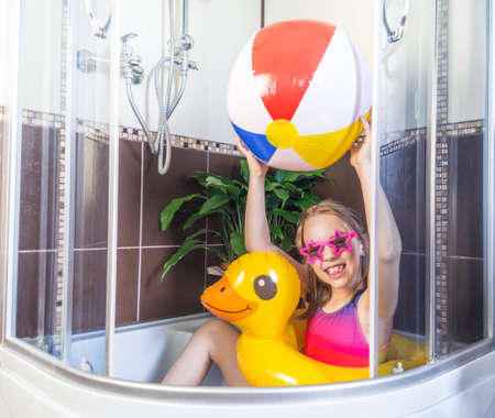 Defocus Little girl sits in the bathroom, imagines that she is resting on the sea. Self isolation due to virus. Stay home and play. Inflatable swimming circle flamingo.の写真素材