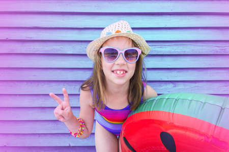 Relax by the pool. Baby on a violet wooden background. Inflatable circle and mattress. Trend color...