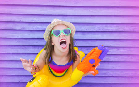 Relax by the pool. Baby on a violet wooden background. Inflatable circle and mattress. Trend color gradient pinkの写真素材