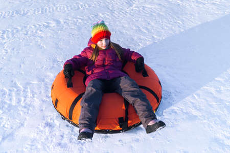 young smiling girl ride sleigh snow tubing hill winter activity concept