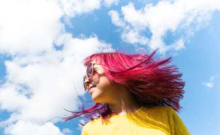 Attractive young girl with pink hair is dancing. Sky background with clouds. Party and fun concept. Kid hair magnificentの写真素材