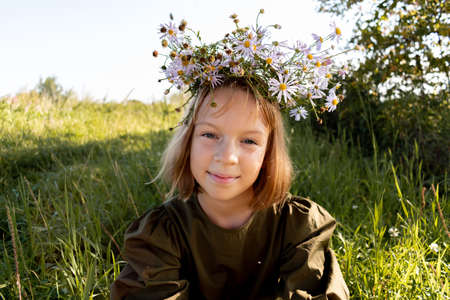 Child with a wreath on his head. Girl in a dress and a straw hat. Glade with flowers. Wellness and freedom concept. Teenager in natureの写真素材
