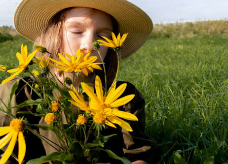 Girl holds a bouquet of yellow wildflowers in her hands. Glade with flowers. Wellness and freedom concept. Teenager in natureの写真素材