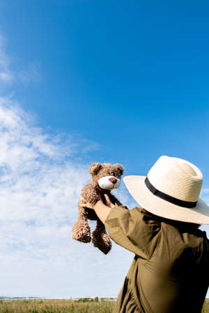 Child plays with a teddy bear. Girl in a dress and a straw hat. Glade with flowers. Wellness and freedom concept. Teenager in natureの写真素材