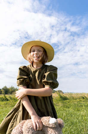 Girl in a linen dress and a straw hat laughs on a flower field. Wicker basket in hands. Wellness and freedom concept. Teenager in natureの写真素材