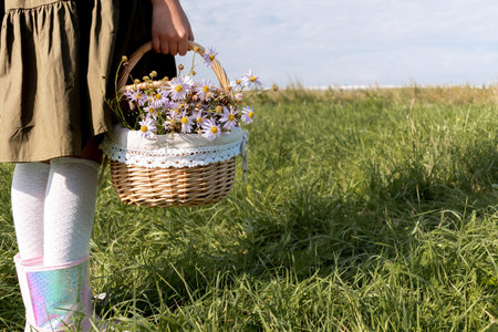 Girl in a linen dress and a straw hat stands on a flower field. Wicker basket in hands. Wellness and freedom concept.の写真素材