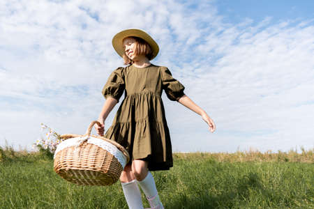 Girl in a linen dress and a straw hat is dancing on a flower field. Wicker basket in hands.の写真素材