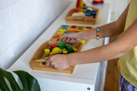 Child takes a tray of Montessori material from the shelf. Homeschooling concept. Toy made of wood cubesの写真素材