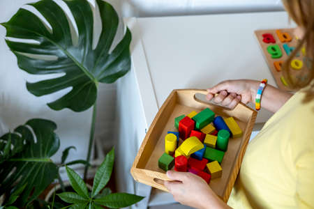 Child takes a tray of Montessori material from the shelf. Homeschooling concept. Toy made of wood cubesの写真素材