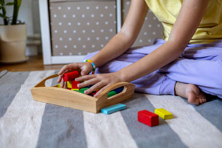 Child collects wooden cubes in a tray. Montessori material. Homeschooling concept. Eco Friendly toyの写真素材