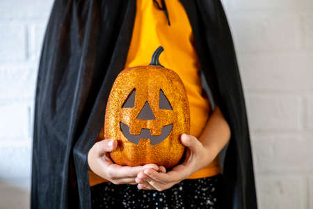 Girl dressed in a witch costume holds a decorative glowing pumpkin in her hands. Halloween celebration concept.の写真素材