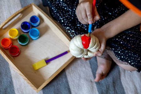 Girl dressed as a witch draws on a pumpkin for the holiday of halloween. Child DIY concept. Home education. Montessori materialの写真素材