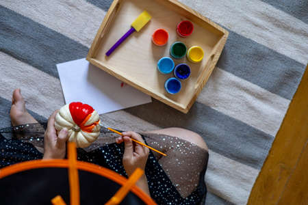 Girl dressed as a witch draws on a pumpkin for the holiday of halloween. Child DIY concept. Home education. Montessori materialの写真素材