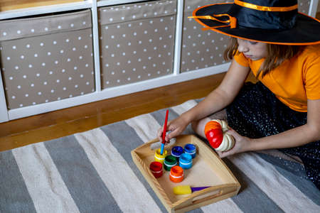 Girl dressed as a witch impregnates a brush with paint. Craft a pumpkin for the holiday of...