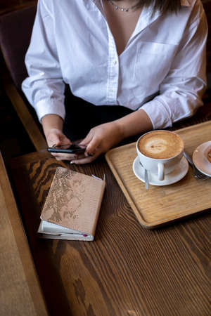 Young woman typing message on mobile phone while drinking coffee. Businesswoman keeps social distanceの写真素材