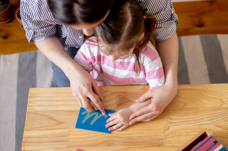 Montessori material. Mom helps her daughter learn letters using the rough alphabet. child toddler girl. concept of learning. Development of motor skills.の写真素材